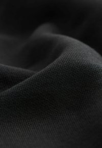 Tela negra que muestra una fina textura acanalada, con caídas suaves y un brillo sutil, indicando un material de peso medio a ligero.