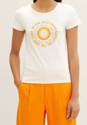 Person trägt ein weißes T-Shirt mit einer lächelnden Sonne und dem Text „Erwarte alle guten Vibes, keine schlechten Tage voraus“ in Orange und Blau.