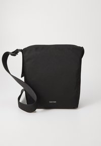 Černá látková taška na rameno s obdélníkovým tvarem, nastavitelným popruhem a malým logem na přední straně. Hladká textura, minimalistický design.