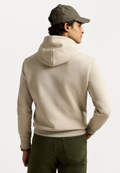 Μπεζ φούτερ με κουκούλα και κορδόνι, πλεγμένα μανίκια και τελείωμα. Φορεμένο με ελαιόχρωμο παντελόνι. Υφασμάτινη επιφάνεια με χαλαρό σχέδιο.