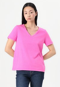 Tricou din bumbac roz cu decolteu în V, mâneci scurte, croială lejeră și detalii de cusătură vizibile. Asortat cu blugi din denim albastru închis.