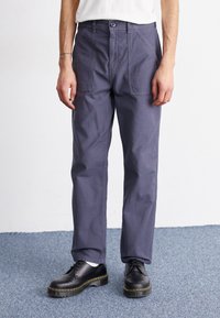 Navy blue trousers in a relaxed fit, made from lightweight fabric. Features front pockets and a button closure. Paired with black lace-up shoes.