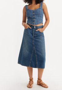 Denimcrop top med knappar, matchad med en högmidjad kjol i knä längd. Båda i medelblå ton; slät textur och avslappnad passform. Bruna sandaletter med remmar.