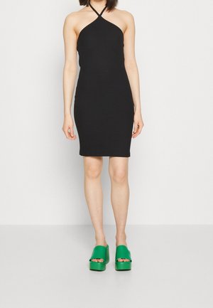 Robe halter noire côtelée avec une silhouette ajustée. Associée à des sandales à plateforme vertes chunky avec une large bride et un design à bout ouvert.