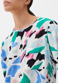 Multikleurige shirt met abstracte patronen in groen, roze, blauw en zwart. Ronde halslijn, losse pasvorm en een detail met een voorzak.