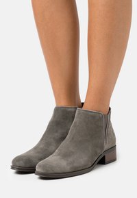 Grå mocka ankelskor med en slät yta, låg klack, elastiska sidopaneler och en dekorativ bakpanel.