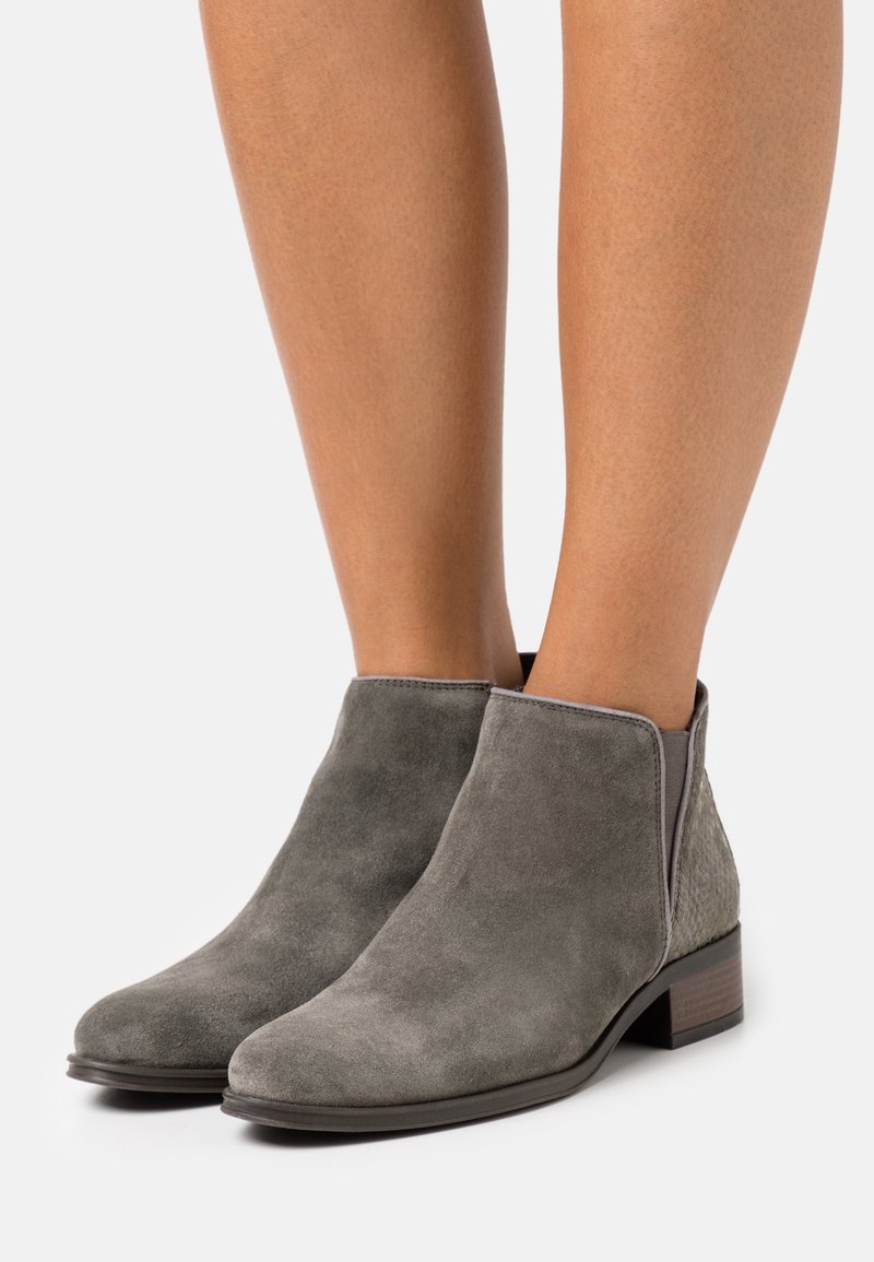 Grå mocka ankelskor med en slät yta, låg klack, elastiska sidopaneler och en dekorativ bakpanel.