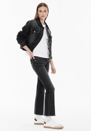 Schwarze Jeansjacke mit Klappentaschen, kombiniert mit schwarzen ausgestellten Jeans und weißen Sneakers. Die Jacke hat einen klassischen Kragen und Knöpfe.