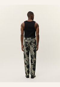 Black sleeveless tank top paired with loose-fitting, patterned trousers in muted green, black, and beige tones. Matte fabric texture.