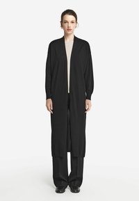 Czarny długi kardigan wykonany z lekkiego, teksturowanego materiału z otwartym przodem i opadającymi rękawami, w połączeniu z czarnymi spodniami o szerokich nogawkach.