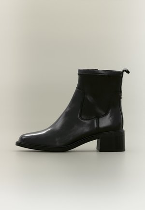 Bottine en cuir noir avec talon bloc, bout arrondi et languette à l'arrière, vue de profil sur un fond neutre.