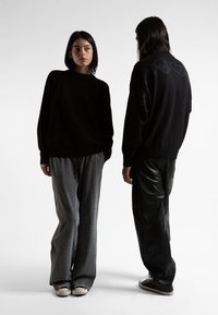 Μαύροι ύφασμα και γκρι παντελόνια με χαλαρή εφαρμογή. Το ένα έχει ματ υφή από δέρμα, ενώ το άλλο διαθέτει μια διακριτική υφασμάτινη σχέδιο.