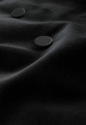 Schwarzer Stoff mit einer weichen Textur, der zwei erhabene runde Knöpfe mit einer strukturierten Oberfläche aufweist, wodurch ein subtiler visueller Kontrast entsteht.