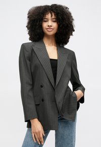 Tmavomodrý blejzer s tenkými prúžkami, dvojradovým zapínaním, klopenými goliermi a dvoma prednými vreckami. Materiál vyzerá hladko a štruktúrovane.