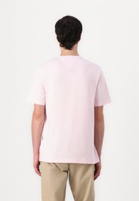 T-shirt en coton rose clair à manches courtes, col rond, avec une couture subtile en forme de V au dos. Associé à un pantalon beige.