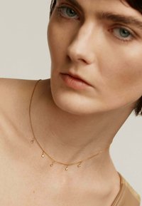 Collar de tono dorado con una cadena delicada y pequeños acentos de colgante espaciados uniformemente. El fondo es neutro y discreto.