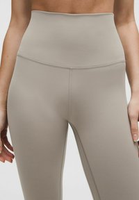 Hoch geschnittene Leggings aus einem hellbeigen Stoff mit glatter Textur. Zu den bemerkenswerten Eigenschaften gehören flache Nähte und ein figurschmeichelndes Design.