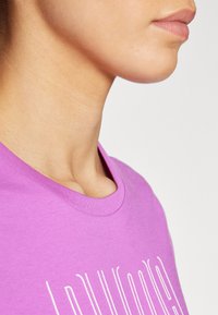 Vijolična bombažna majica s krožnim izrezom, s postopkom bele barve na sprednji strani. Gladka tekstura, sproščen fit in kratki rokavi.