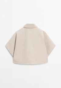 Veste courte cape beige à manches larges et petit col, vue de dos sur un fond blanc uni.