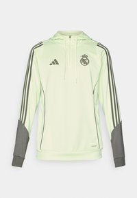 Lys grønn hettegenser med grå detaljer, har tre svarte striper på ermene, Adidas-logo og Real Madrid-emblemet.