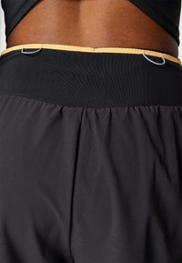 Pantalones cortos deportivos negros con una textura suave, cinturilla elástica con un acento amarillo y un pequeño lazo de metal para accesorios.