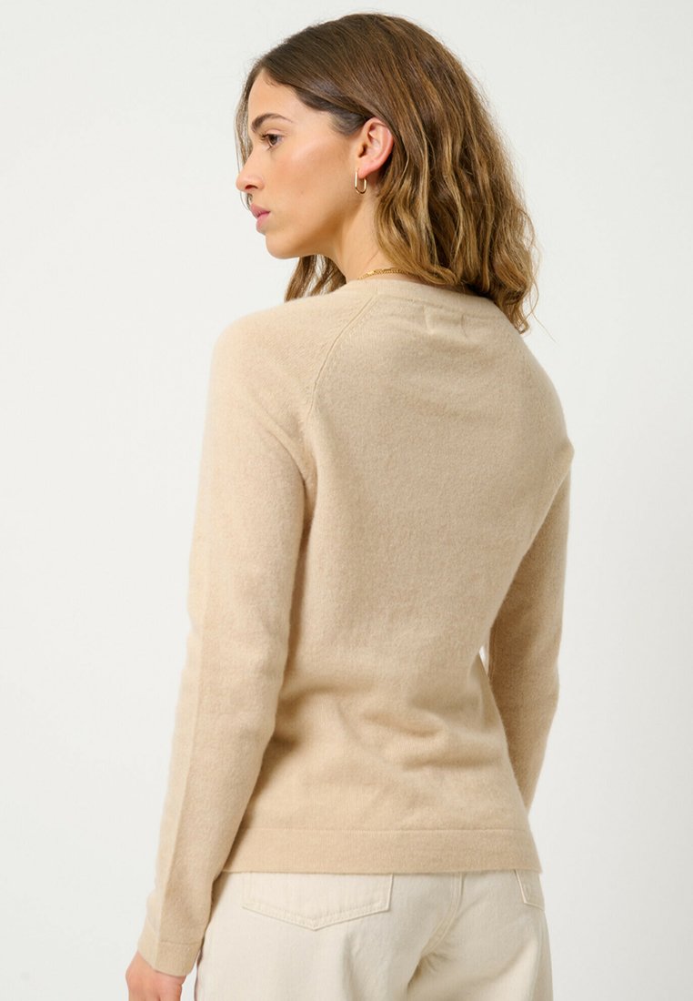 Pull en cachemire beige à manches longues et col rond, avec une texture subtile et une coupe ajustée.