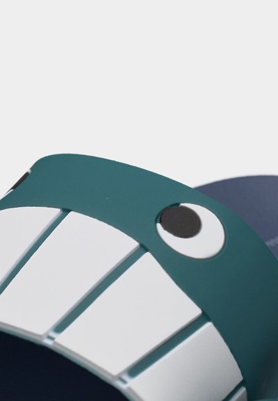 Κοντινή λήψη ενός πετρόλ παντόφλας με σχέδιο καρτούν ματιών και μεγάλα λευκά δόντια στο μπροστινό μέρος.