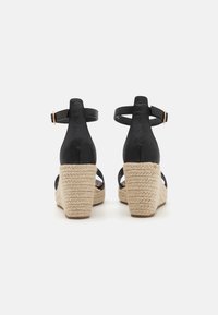 Sorte lærwedge-sandaler med en vevet jute-plattform, som har ankelstropper og en glatt finish. Hælhøyden er merkbar.