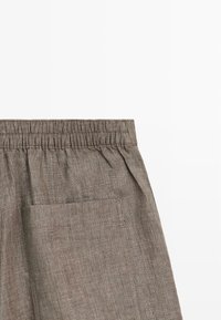 Bruine linnen broek met een elastische tailleband en een grote rechthoekige zak aan de zijkant.