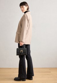 Blazer beige avec une coupe décontractée, col roulé noir, jeans évasés foncés et chaussures à plateforme noires. Tient un petit sac à main noir avec des garnitures dorées.