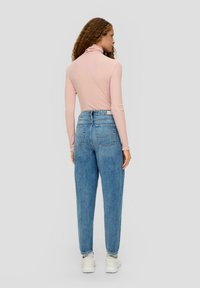 Lichtroze, lang mouwturtleneck genaamd, gecombineerd met comfortabele blauwe denim jeans. Witte sneakers en subtiele details op de achterzakken zijn zichtbaar.