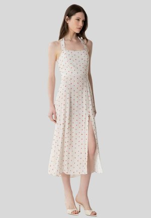 Donna che indossa un vestito midi bianco senza maniche con una piccola stampa floreale rossa e uno spacco frontale, abbinato a tacchi beige aperti sulle dita.