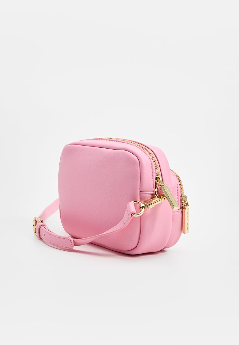 Różowa skórzana torebka crossbody o prostokątnym kształcie, gładkiej fakturze, podwójnym zamku błyskawicznym, złotymi akcentami i regulowanym paskiem.