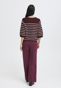 Knitted burgundy sweater with beige stripes, three-quarter sleeves, paired with matching wide-leg burgundy pants and black shoes.