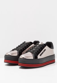 Baskets plateforme en argent métallisé et noir avec des accents de rayures rouges, présentant une texture lisse, des matériaux contrastants et un design à bout rond.