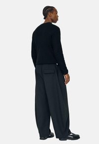 Sort strikket sweater med rund halsudskæring, kombineret med brede sorte bukser med baglomme, båret sammen med sort fodtøj.