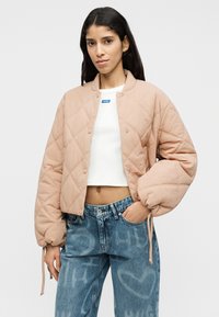 Ραφτό, ροδακινί μπουφάν bomber με στρογγυλή γιακά, κουμπιά με κλικ και ελαστικά μανίκια. Συνδυασμένο με τζιν ψηλοκάβαλα.