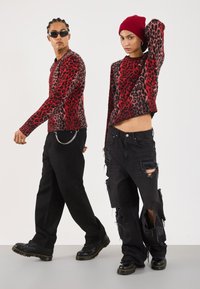 Jerséis de leopardo rojo y negro con puños acanalados, combinados con jeans negros desgastados. Ambos llevan botas negras y accesorios.