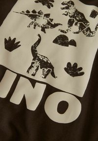 Rjav bombaž s potiskom dinozavrov, ki vključuje črne silhuete, vključno z T-Rexom in stegosaurusom, ter belo blokovno pisavo.