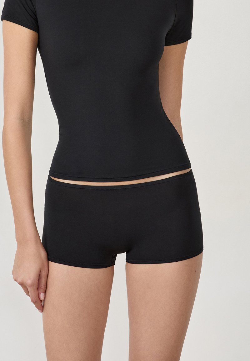 Haut noir ajusté à manches courtes associé à un short en mélange de modal noir. Texture douce, coutures minimes et design épuré.