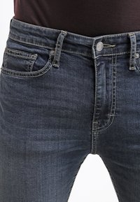 Jeans de mezclilla azul oscuro con corte recto, que cuentan con cinco bolsillos, cierre con botón de metal y un sutil desteñido en las piernas.