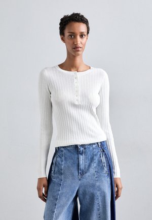 Hvit ribbestrikket langermet skjorte med rund hals og en rad med fem knapper foran, kombinert med høyhanskede denimbukser.