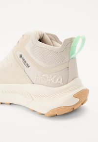 Beige turistsko sko med Gore-Tex overdel, struktureret mesh, en grøn træksløjfe og en mønstret gummisål for godt greb.