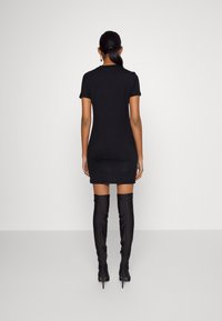 Černé šaty s krátkým rukávem, přiléhavé, po kolena, spárované s černými vysokými kozačkami na podpatku, hladká textura, minimalistický design.