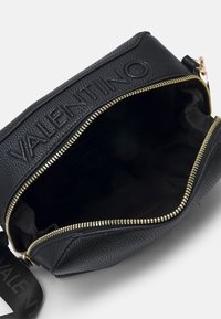 Black leather bag with textured finish, gold zipper, and embossed lettering. Interior in solid black fabric with zippered pocket compartment.