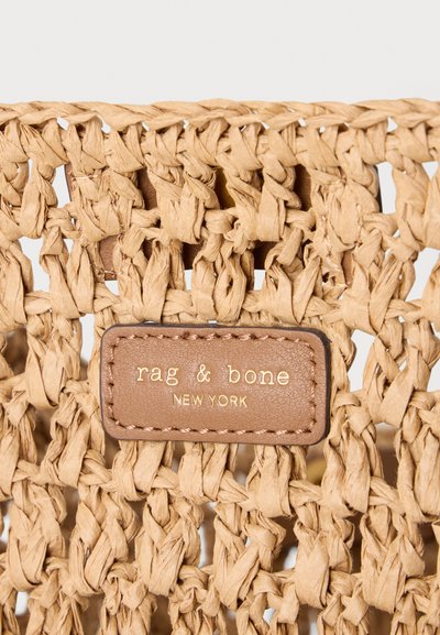 Gros plan d’un sac en fibres naturelles tissées avec une étiquette en cuir cousue indiquant « rag & bone NEW YORK » en lettres dorées.