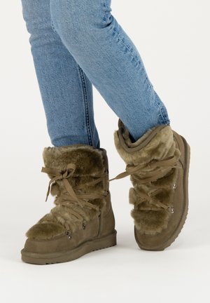 Brown suede ankle boots with fur lining, ribbon laces, and metal eyelets. The textured upper features soft fur accents at the top.