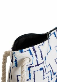 Borsa intrecciata bianca con motivi geometrici blu e viola, dotata di apertura superiore con cerniera e maniglie in corda. Fodera interna nera.