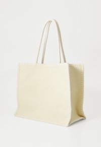 Borsa tote in tessuto beige con bordi cuciti, due manici a forma di corda, base rettangolare, texture morbida e senza elementi metallici o motivi visibili.