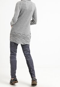 Grå stickad lång cardigan med en texturerad, vågig kant; matchad med mörk marinblå, figursydda byxor och svarta snörskor.